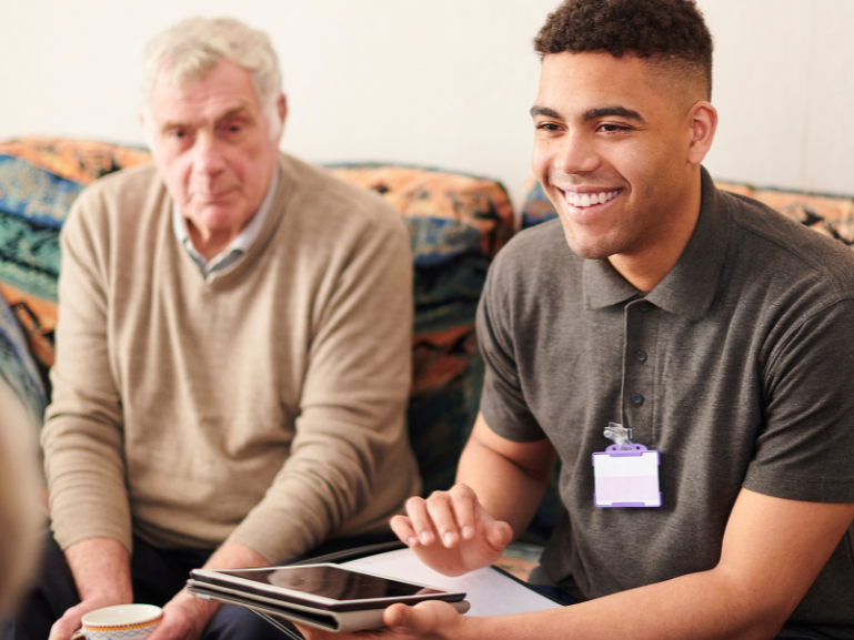 Care image male staff sitting on sofa smiling, client to left and person opposite