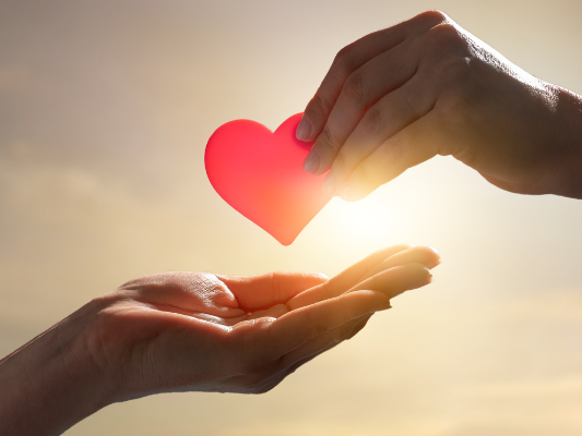 Sky background with one hand holding a heart, passing onto another person's hand